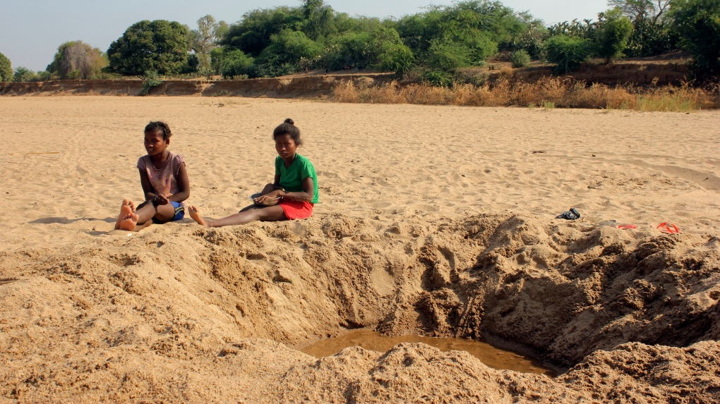 Children sit by a dug out water hole