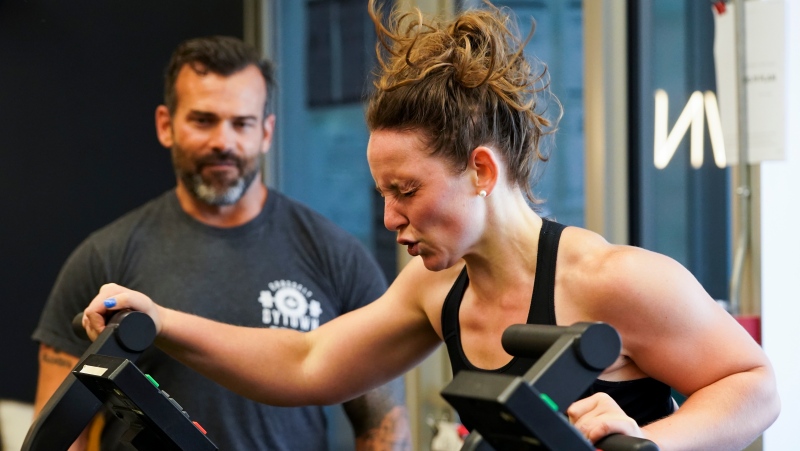 Lili Johanis works out as coach and owner Everett Sloan of Crossfit Bytown looks on as patrons return to the gym with Ontario enters phase 3 of reopening during the COVID-19 pandemic in Ottawa on Friday, July 16, 2021. (Sean Kilpatrick /THE CANADIAN PRESS)