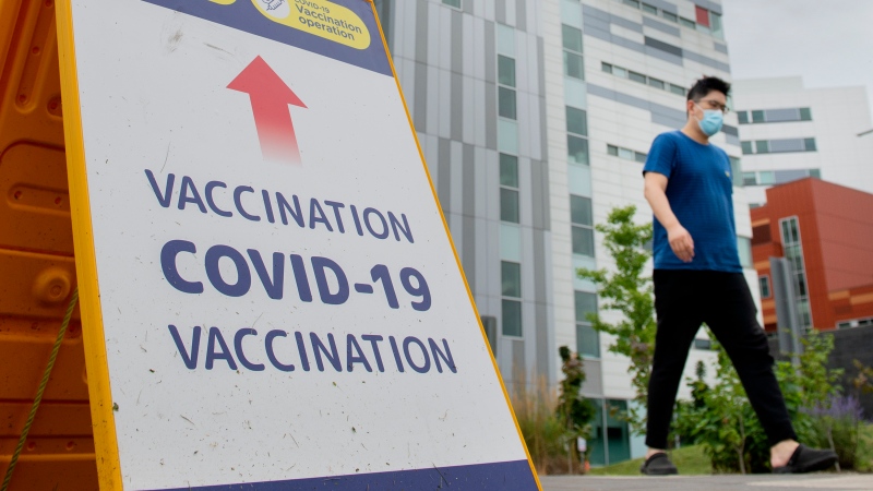 A man wears a face mask as he walks by a COVID-19 vaccination sign in Montreal, Sunday, August 1, 2021, as the COVID-19 pandemic continues in Canada and around the world. THE CANADIAN PRESS/Graham Hughes