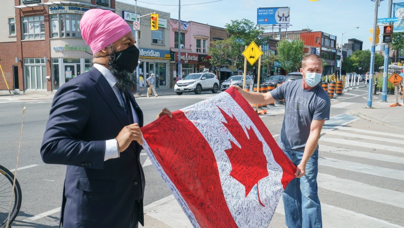 NDP Leader Jagmeet Singh stretches out a supporter's Canadian flag for a photo during a campaign stop in Toronto, on Monday, August 16, 2021. THE CANADIAN PRESS/Paul Chiasson 