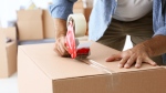 A man tapes up a moving box in a stock image. 