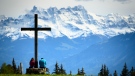 People take a break under a cross in a field and enjoy a spring weather day in front of the Swiss Alps mountains (Les Dents du Midi), in Les Pleiades Blonay above Montreux, Switzerland, Sunday, May 23, 2021. (Laurent Gillieron/Keystone via AP)