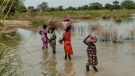 Children carry bags on their head as they walk the flooded fields near Malualkon in Northern Bahr el Ghazal State, South Sudan, Wednesday, Oct. 20, 2021. (AP Photo/Adrienne Surprenant)