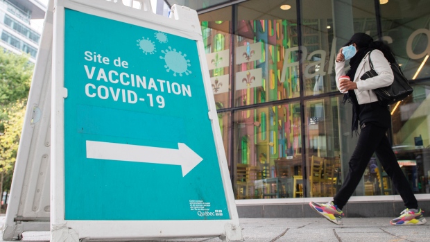 A person removes their face mask as they walk by a sign advertising a COVID-19 vaccination site, in Montreal, Sunday, Oct. 3, 2021. THE CANADIAN PRESS/Graham Hughes 