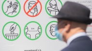 A man wears a face mask as he looks at a sign illustrating COVID-19 preventative measures in Montreal, April 24, 2021. THE CANADIAN PRESS/Graham Hughes