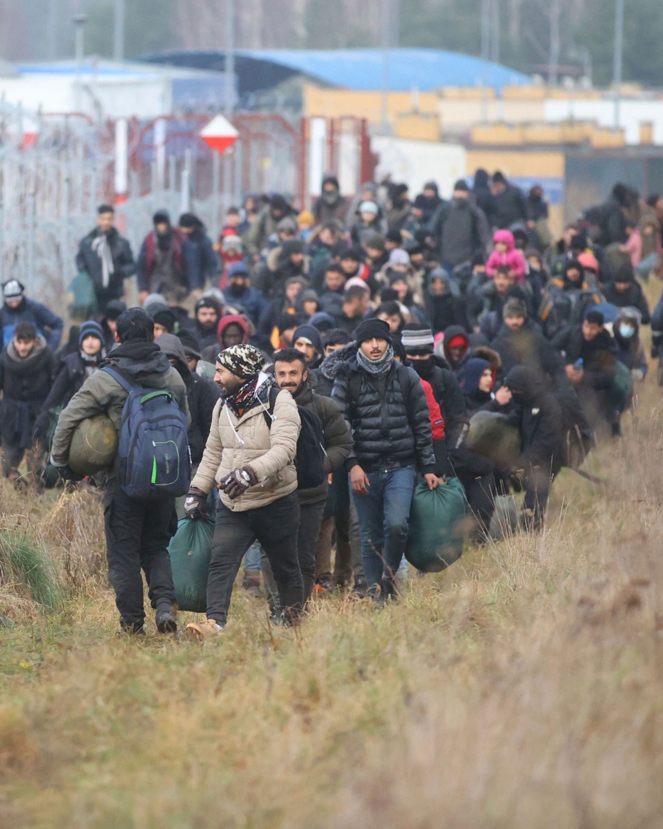 Migrants walk along barbed wire