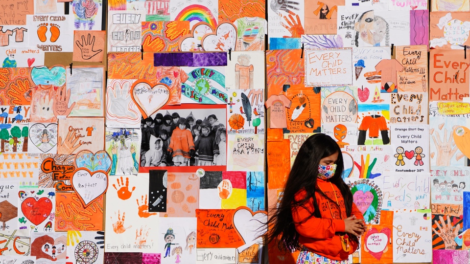 A child stands by a wall of "Every Child Matters,"