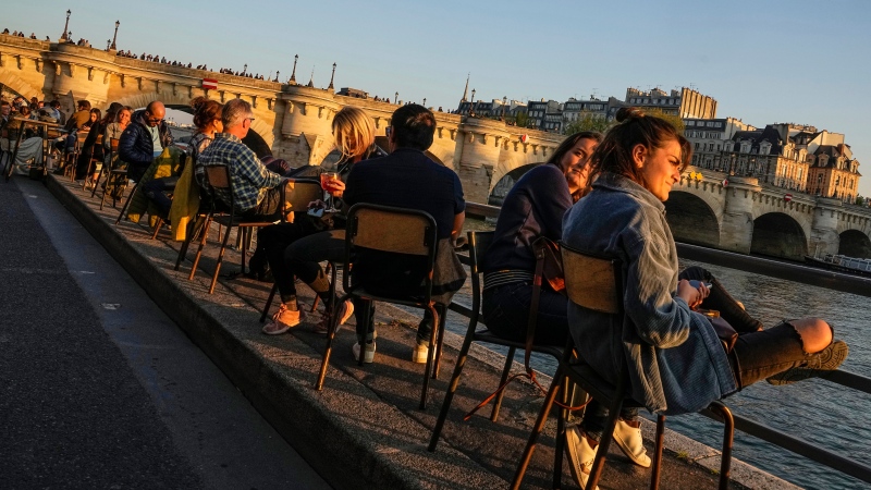 People sit at a cafe along the seine river bank by the setting sun in Paris, Saturday, Oct. 9, 2021. (AP Photo/Michel Euler) 