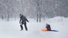 FILE: A woman pulls a child on a sled as snow falls in Montreal, Saturday, February 27, 2021. THE CANADIAN PRESS/Graham Hughes