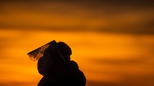 A woman wearing a face mask and face shield to curb the spread of COVID-19 is silhouetted during sunset at Ambleside Beach in West Vancouver, on Sunday, Jan. 9, 2022. (Darryl Dyck /  THE CANADIAN PRESS)