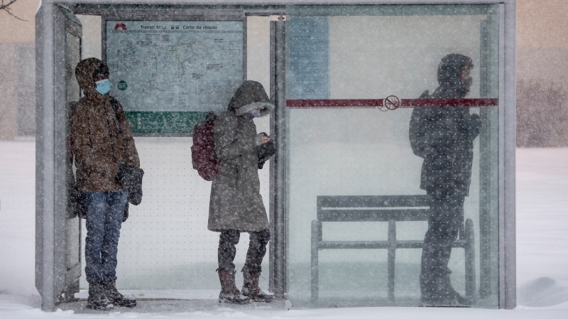 People take shelter from heavy snow and driving wind as they wait for a bus in Ottawa, on Monday, Jan. 17, 2022. A blizzard warning is in effect for the region with Environment Canada predicting between 25 to 40 cm of snow. (Justin Tang /THE CANADIAN PRESS)