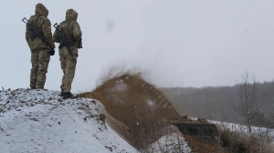 In this image provided by the Ukrainian Board Guard Press Office, Ukrainian border guards watch as a special vehicle digs a trench on the Ukraine-Russia border close to Sumy, Ukraine, Tuesday, Dec. 21, 2021. (Ukrainian Board Guard Press Office via AP) 