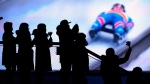 Spectators are silhouetted by a large screen showing the competition as they cheer during the men's race at the Luge World Cup, a test event for the 2022 Winter Olympics, at the Yanqing National Sliding Center in Beijing, on Nov. 20, 2021. (Mark Schiefelbein / AP) 