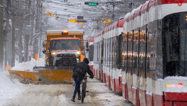 A cyclict hops off his bike to get out of the way of a snow plow while making his way past dozens of stranded streetcars during a severe winter storm in Toronto on Monday January 17, 2022. THE CANADIAN PRESS/Frank Gunn 