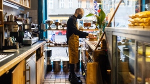 Side view of a male barista wearing protective face mask and apron working in a bakery. (Getty Images) 