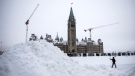 A person makes a video call from their phone as they pass a pile of snow in front of Parliament Hill's Centre Block in Ottawa after a winter storm on Monday, Jan. 17, 2022. THE CANADIAN PRESS/Justin Tang