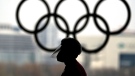 A person wearing a face shield walks past the Olympic rings inside the main media centre at the 2022 Winter Olympics, January 19, in Beijing. (David J. Phillip/AP)