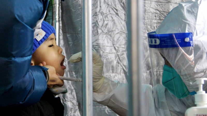 In this photo released by Xinhua News Agency, a child gets a throat swab for the COVID-19 test at a residential area in Fengtai District in Beijing, Sunday, Jan. 23, 2022. (Tang Rufeng/Xinhua via AP)
