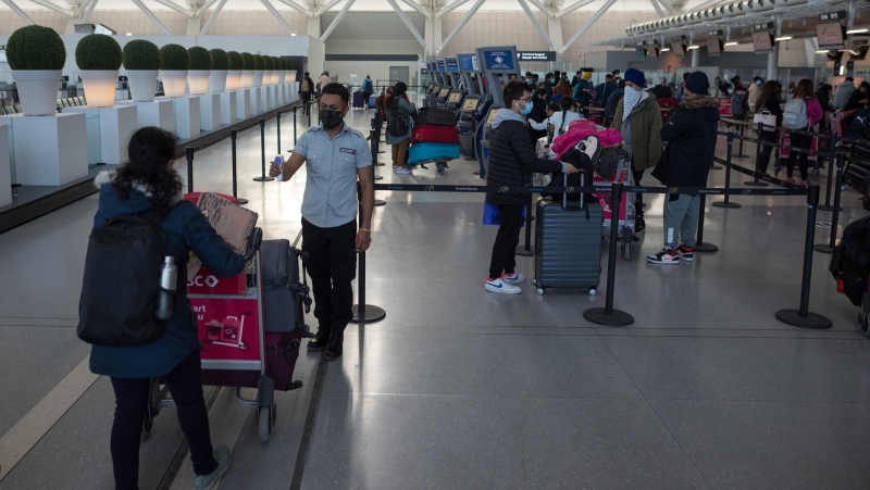 A worker checks the temperature of a traveler departing from Toronto Pearson International Airport, on Thursday, December 16, 2021. THE CANADIAN PRESS/Tijana Martin