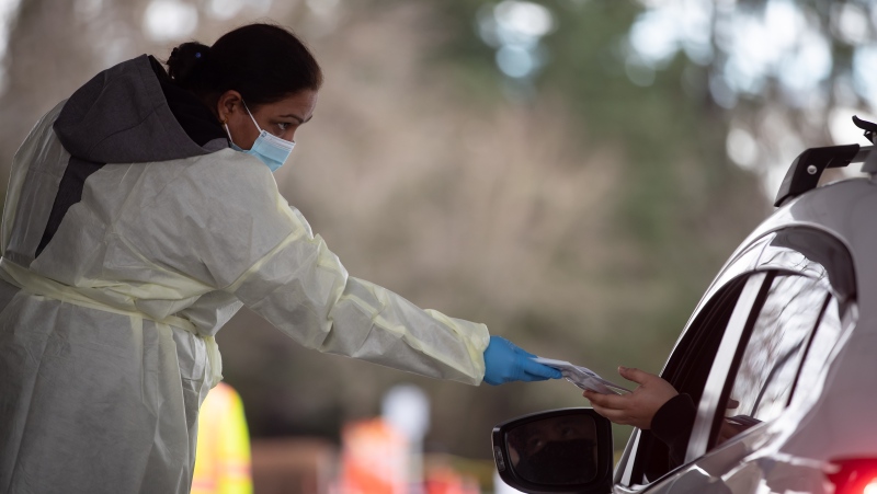 Fraser Health employee Amarjeet Jammu hands a COVID-19 rapid test kit to a motorist at a drive-thru pick up site in Surrey, B.C., on Thursday, January 20, 2022. THE CANADIAN PRESS/Darryl Dyck 