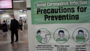 People wearing face masks pass by a poster reminding precautions against COVID-19 at a subway station in Seoul, South Korea, on Jan. 25, 2022. (AP Photo/Ahn Young-joon)