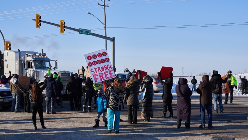 Protesters of COVID-19 restrictions, and supporters of Canadian truck drivers protesting the COVID-19 vaccine mandate cheer on a convoy of trucks on their way to Ottawa, on the Trans-Canada Highway west of Winnipeg, Manitoba, Tuesday January 25, 2022. THE CANADIAN PRESS/David Lipnowski 