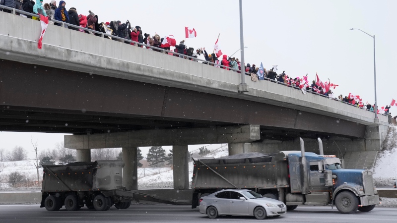 Supporters holding Canadian flags stand on an overpass and cheer as trucks pass by while honking their horns as they travel on Highway 400 in Toronto on Thursday Jan. 27, 2022. THE CANADIAN PRESS/Frank Gunn 