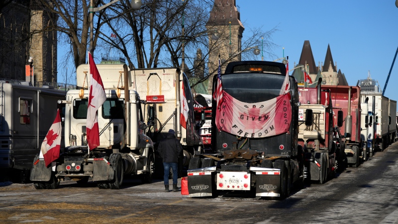A person walks among trucks as Wellington Street is lined with trucks once again after city officials negotiated to move some trucks towards Parliament and away from downtown residences, on the 18th day of a protest against COVID-19 measures that has grown into a broader anti-government protest, in Ottawa, on Monday, Feb. 14, 2022. (Justin Tang/THE CANADIAN PRESS)