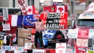 A protester dances on a concrete jersey barrier in front of vehicles and placards on Rideau Street, on the 20th day of a protest against COVID-19 measures that has grown into a broader anti-government protest, in Ottawa, on Wednesday, Feb. 16, 2022. (Justin Tang/THE CANADIAN PRESS)