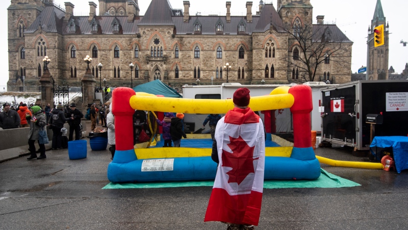 A protester wearing a Canadian flag takes a photo of children playing in an inflatable bouncy castle on Wellington Street across from Parliament’s West Block on the 21st day of a protest against COVID-19 measures that has grown into a broader anti-government protest, in Ottawa, on Thursday, Feb. 17, 2022. (THE CANADIAN PRESS/Justin Tang)