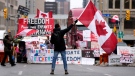 A protester waves a Canadian flag in front of parked vehicles on Rideau Street on the 15th day of a protest against COVID-19 measures that has grown into a broader anti-government protest, in Ottawa, Friday, Feb. 11, 2022. THE CANADIAN PRESS/Justin Tang