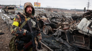 An armed man stands by the remains of a Russian military vehicle in Bucha, close to the capital city Kyiv, Ukraine, on March 1, 2022. (AP Photo/Serhii Nuzhnenko)