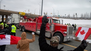 A truck passes Ontario Provincial Police officers and demonstrators in opposition to COVID-19 mandates on the Toronto-bound QEW highway after crossing the Peace Bridge in Fort Erie, Ontario Saturday, February 12, 2022. THE CANADIAN PRESS/Aaron Lynett 