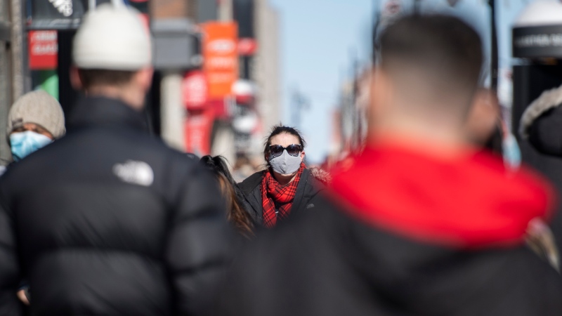 People wear face masks as they walk along a street in Montreal, Sunday, February 21, 2021, as the COVID-19 pandemic continues in Canada and around the world. THE CANADIAN PRESS/Graham Hughes