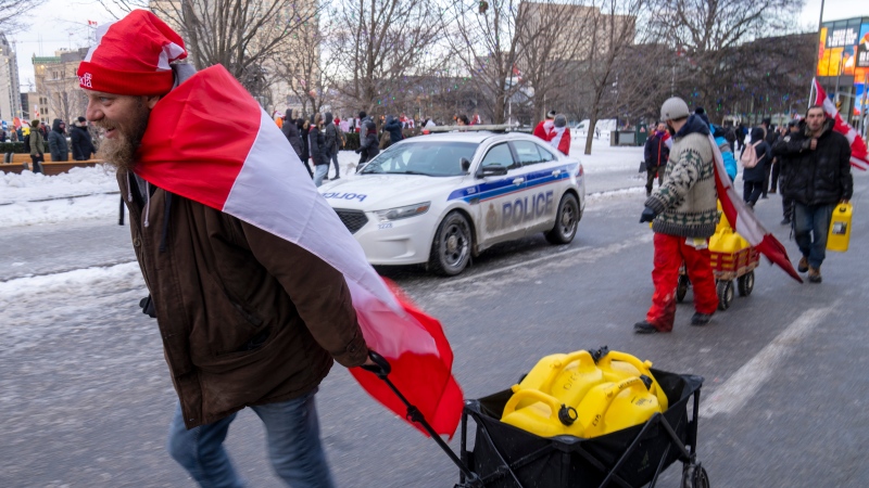 Protesters haul fuel past a police car during the COVID-19 anti-mandate protest on Parliament Hill in Ottawa on Saturday, February 12, 2022. (Frank Gunn/THE CANADIAN PRESS)