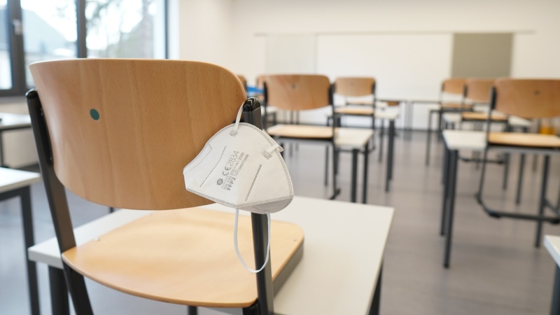 An mask rests on the back of a chair in an empty classroom. (Photo by Marco Fileccia on Unsplash)