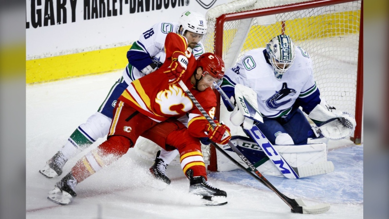 Vancouver Canucks centre Jason Dickinson, left, checks Calgary Flames centre Blake Coleman, centre, as he tries to score on goalie Thatcher Demko during third period NHL hockey action in Calgary on April 23, 2022. Jeff McIntosh/The Canadian Press