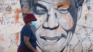 A woman wearing a mask walks past a mural of former South Africa's president Nelson Mandela, in Katlehong, east of Johannesburg, South Africa, Friday, April 29, 2022. (AP Photo/Themba Hadebe) 