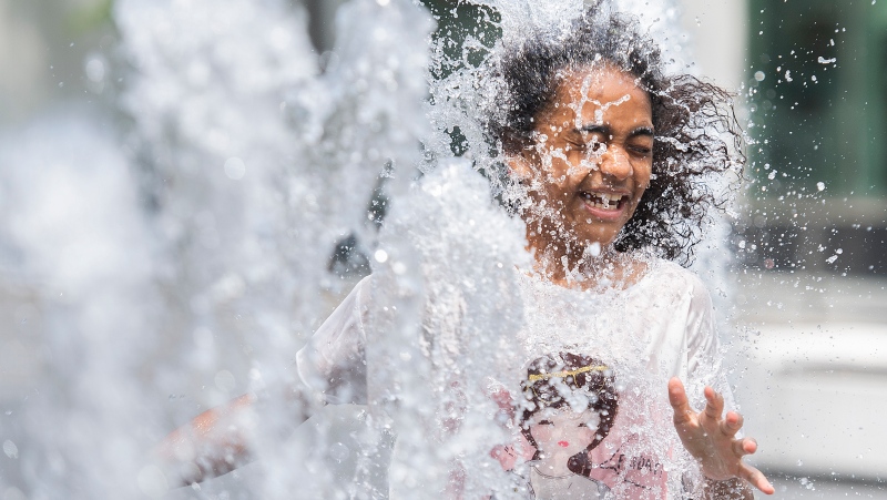 FILE: Emily Adejor (10) beats the heat as she runs through a water fountain in Montreal, Sunday, June 6, 2021. THE CANADIAN PRESS/Graham Hughes