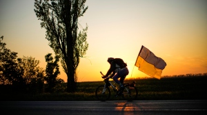 A man rides a bicycle with a Ukrainian flag on the road between Odesa and Mykolaiv, southern Ukraine, Saturday, May 14, 2022. (AP Photo/Francisco Seco)