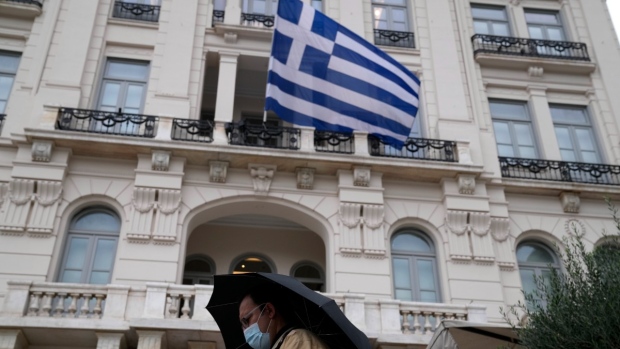 A man wearing a face mask to protect against coronavirus walks outside an electronic store as a Greek flag waves in Athens, Greece, Nov. 2, 2021. (AP Photo/Thanassis Stavrakis)