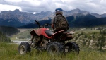 A stock photo of a man looking at the mountains on his ATV.