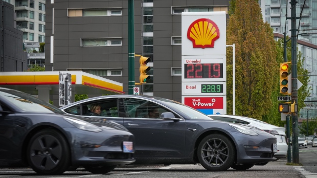 Three Tesla electric vehicles drive past a sign displaying the price of a litre of regular gasoline after it reached a new high of $2.28 in Vancouver on Saturday, May 14, 2022. (THE CANADIAN PRESS/Darryl Dyck)