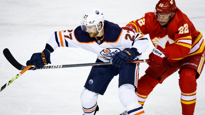 Edmonton Oilers' Brett Kulak, left, is checked by Calgary Flames' Trevor Lewis during third period NHL hockey action in Calgary, Saturday, March 26, 2022.THE CANADIAN PRESS/Jeff McIntosh 