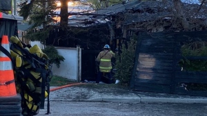 A Calgary Fire Department members stands next to a damaged home and charred fence following a May 17 fire along Simons Crescent N.W. in Thorncliffe.