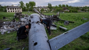 Oleksiy Polyakov, right, and Roman Voitko check the remains of a destroyed Russian helicopter lie in a field in the village of Malaya Rohan, Kharkiv region, Ukraine, May 16, 2022. (AP Photo/Bernat Armangue)