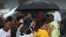 Bystanders gather under an umbrella as rain rolls in after a shooting at a supermarket on Saturday, May 14, 2022, in Buffalo, N.Y. Officials said the gunman entered the supermarket with a rifle and opened fire. Investigators believe the man may have been livestreaming the shooting and were looking into whether he had posted a manifesto online. (AP Photo/Joshua Bessex)