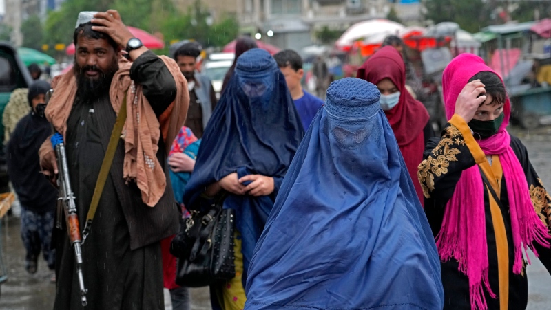 Afghan women walk through the old market as a Taliban fighter stands guard, in downtown Kabul, Afghanistan, Tuesday, May 3, 2022. (AP Photo/Ebrahim Noroozi)