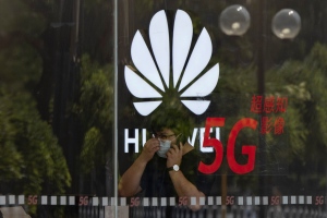 A worker wearing a mask to curb the spread of the coronavirus speaks on the phone near the Huawei logo in a store in Beijing on Wednesday, July 15, 2020. China's government accused Britain on Wednesday of colluding with Washington to hurt Chinese companies after tech giant Huawei was blocked from working on a next-generation mobile phone network. (AP Photo/Ng Han Guan)