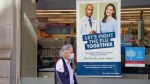 A pedestrian walks by a sign in a store window encouraging people to receive a seasonal flu shot in Toronto, Oct. 19, 2021. THE CANADIAN PRESS/Evan Buhler